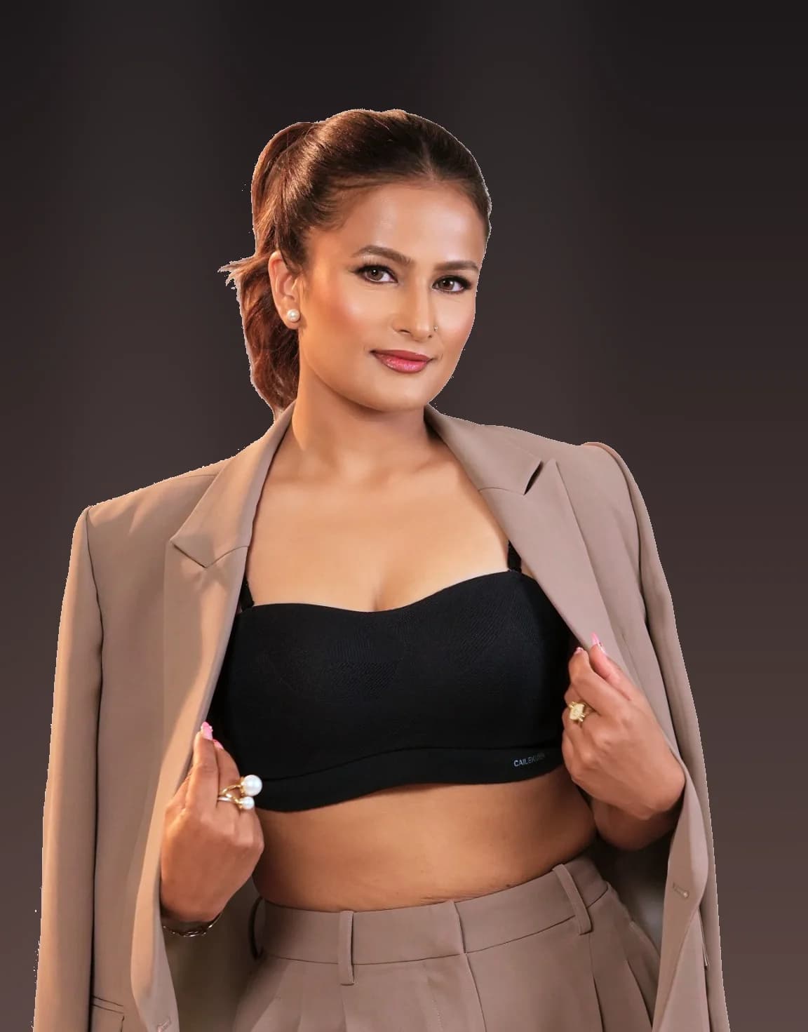 Janu in a tailored beige suit worn open, against a deep studio backdrop