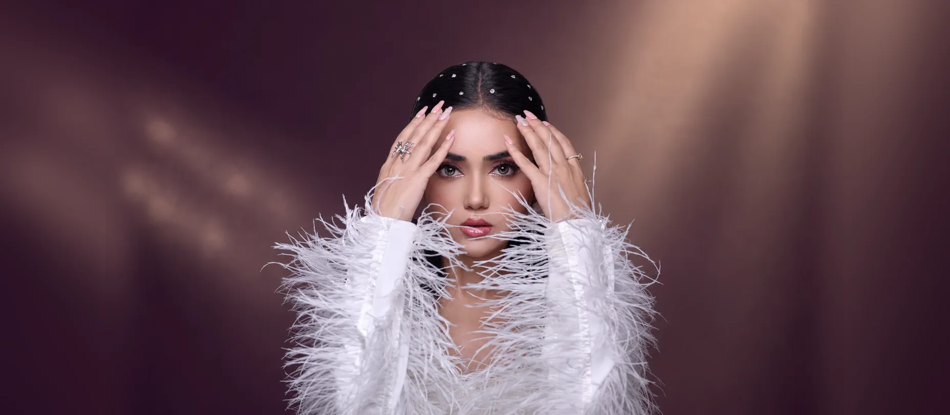 A guest in a white feathered dress and crystal headband, party makeup by NJS